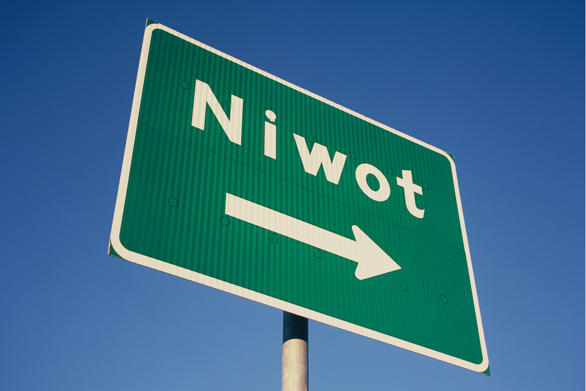 Green highway sign reading 'Niwot' with a right-pointing arrow against a deep blue sky.