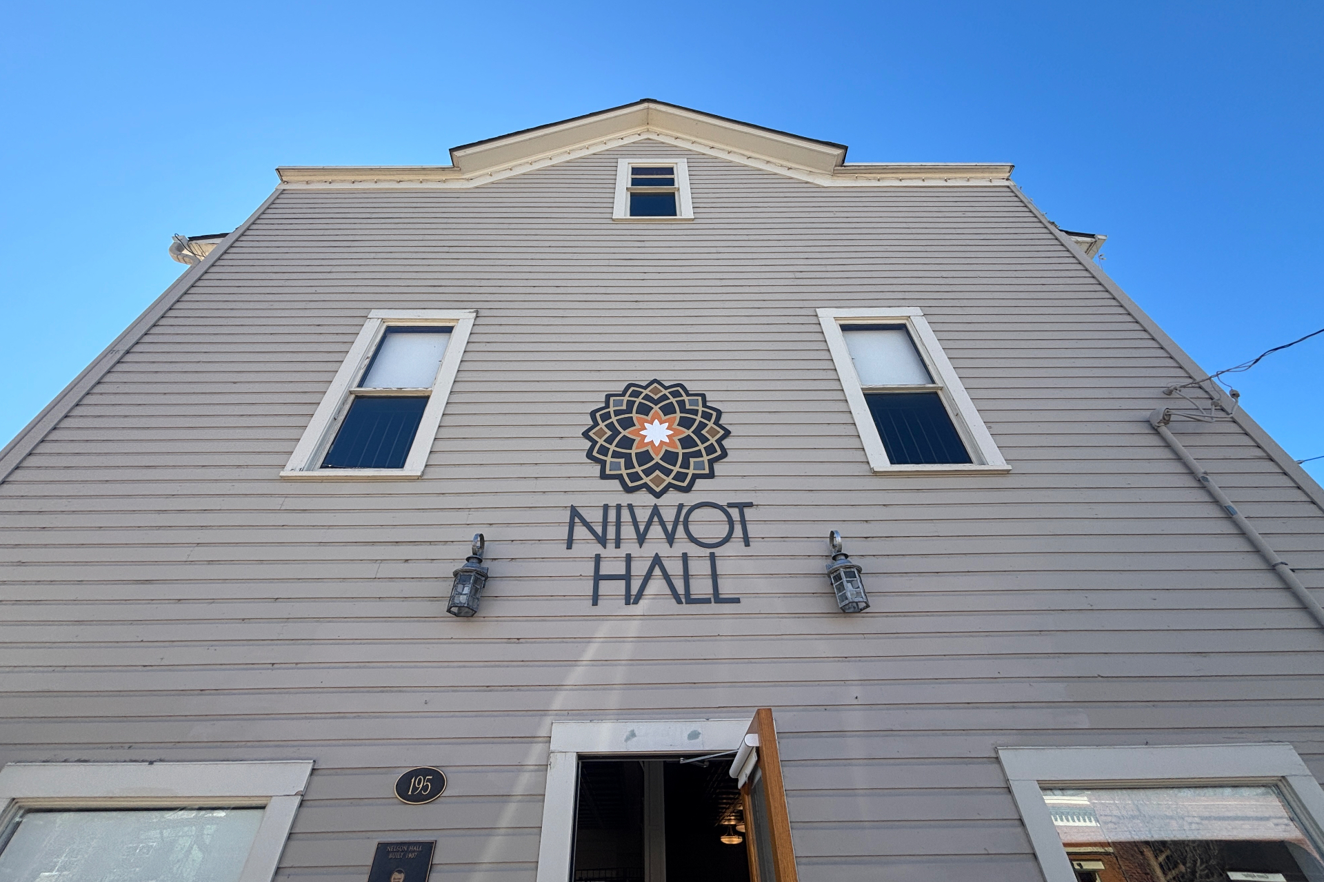 Niwot Hall facade with the Niwot Hall sign and decorative emblem, against a clear blue sky.